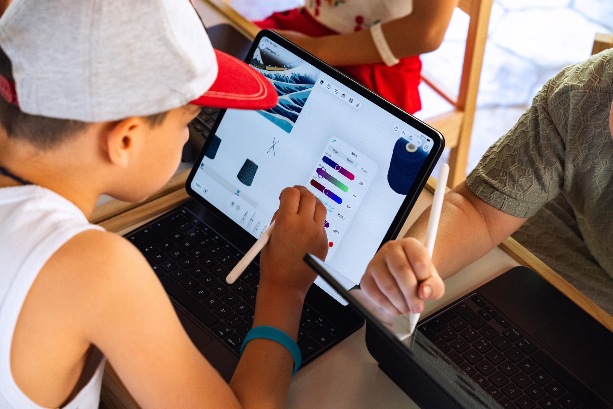 A child explores colour on an iPad with an Apple Pencil, with bobbins and a wave image on screen.