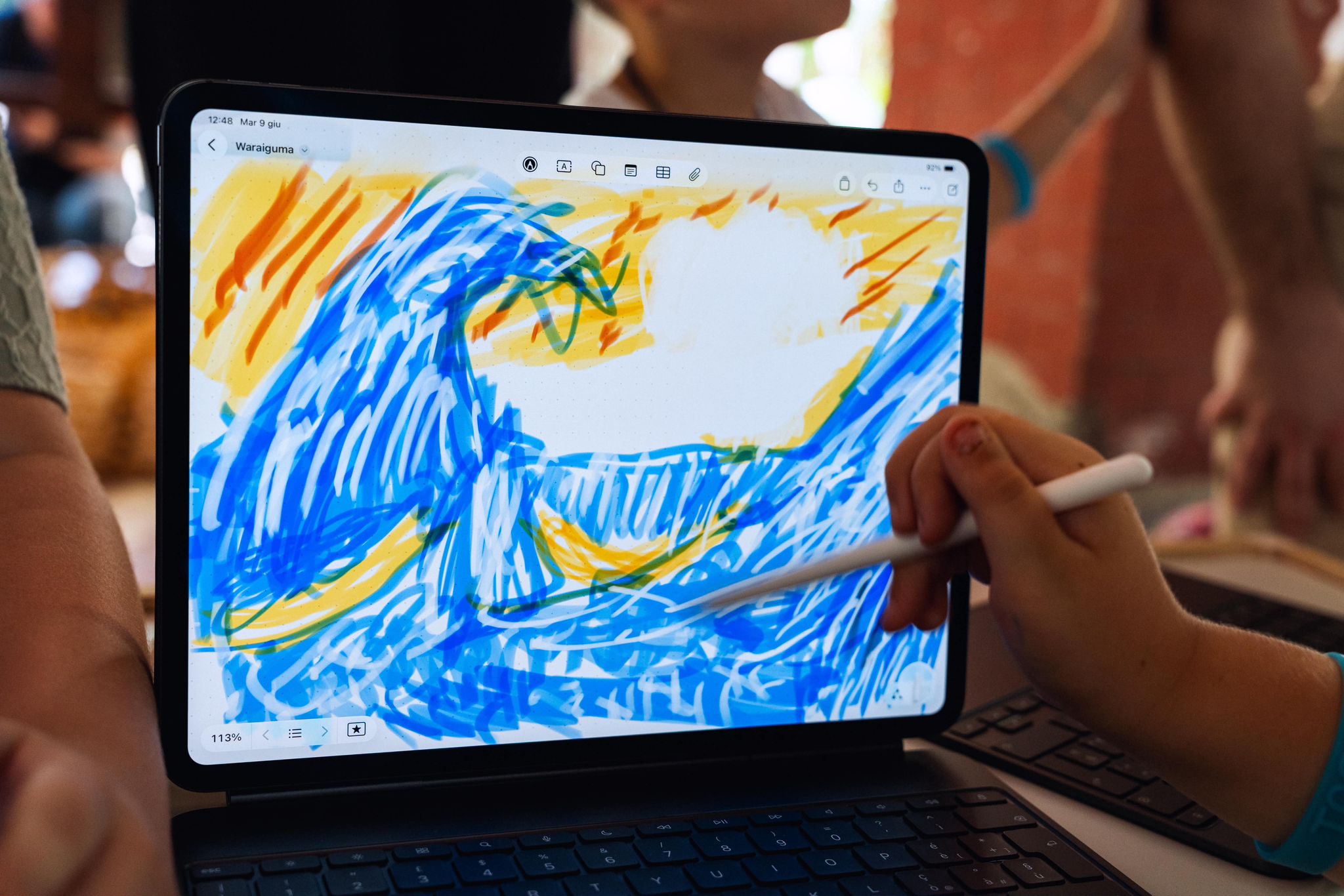 A child draws blue and yellow waves on an iPad with an Apple Pencil.