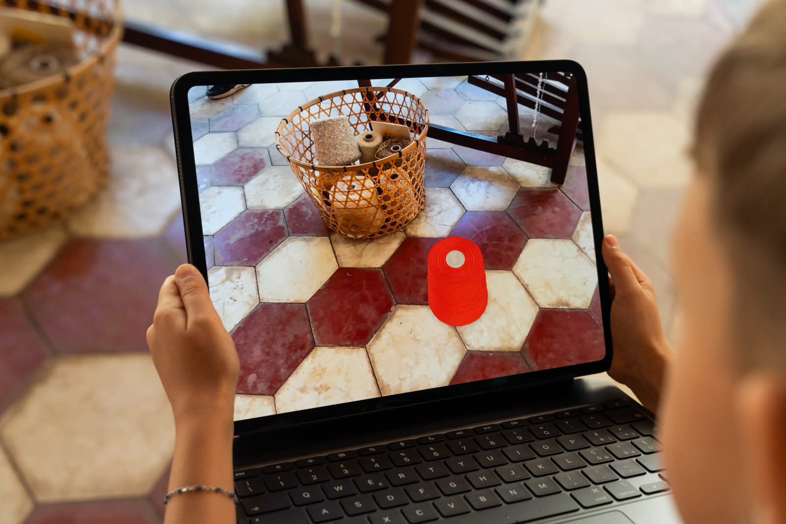A child views a red digital bobbin in augmented reality beside a basket of real yarn.